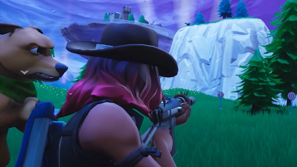 A Fortnite character dressed in a cowboy hat, with a dog on their back, shooting at a practice target by a hill and some trees.