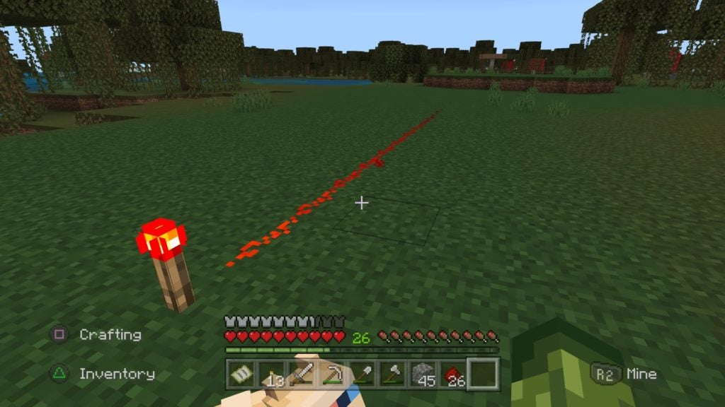 A redstone torch planted in the grass in front of the player. It is illuminating some of a like of redstone dust in front of it.