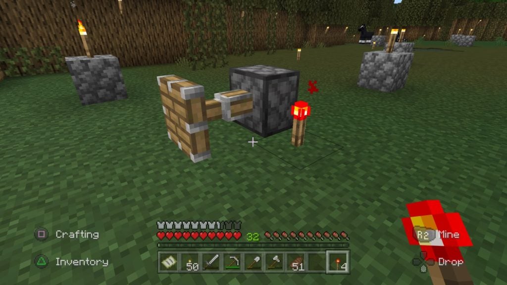 There is an activated piston on the grass next to a lit redstone torch. The wooden head of the piston is extended away from its stone body.