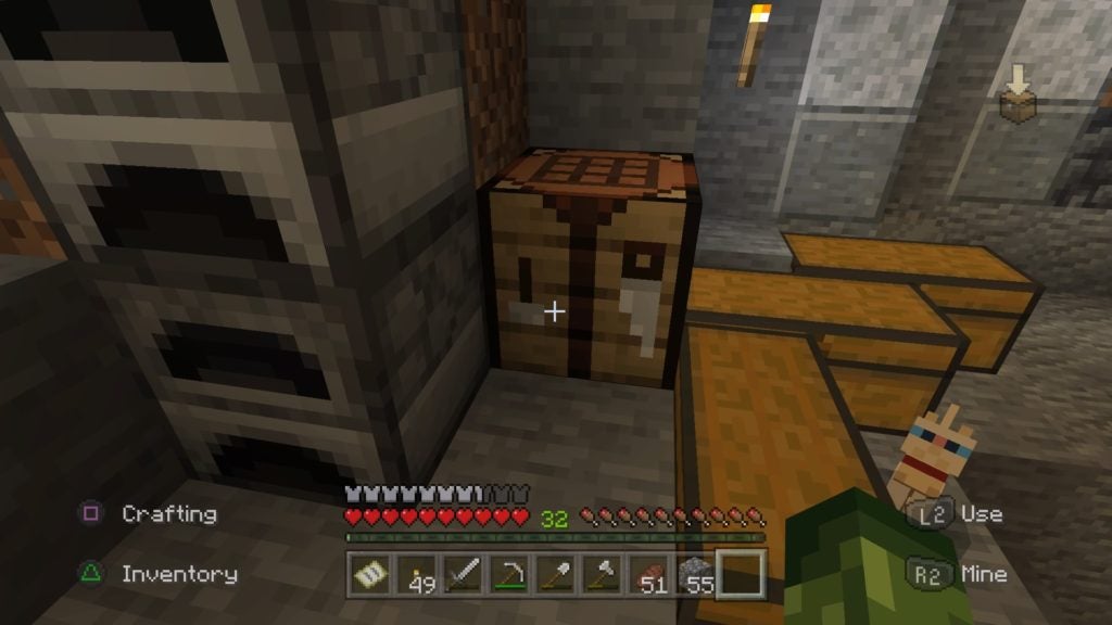 A crafting table in the corner. It is brown and has some tools on its side.