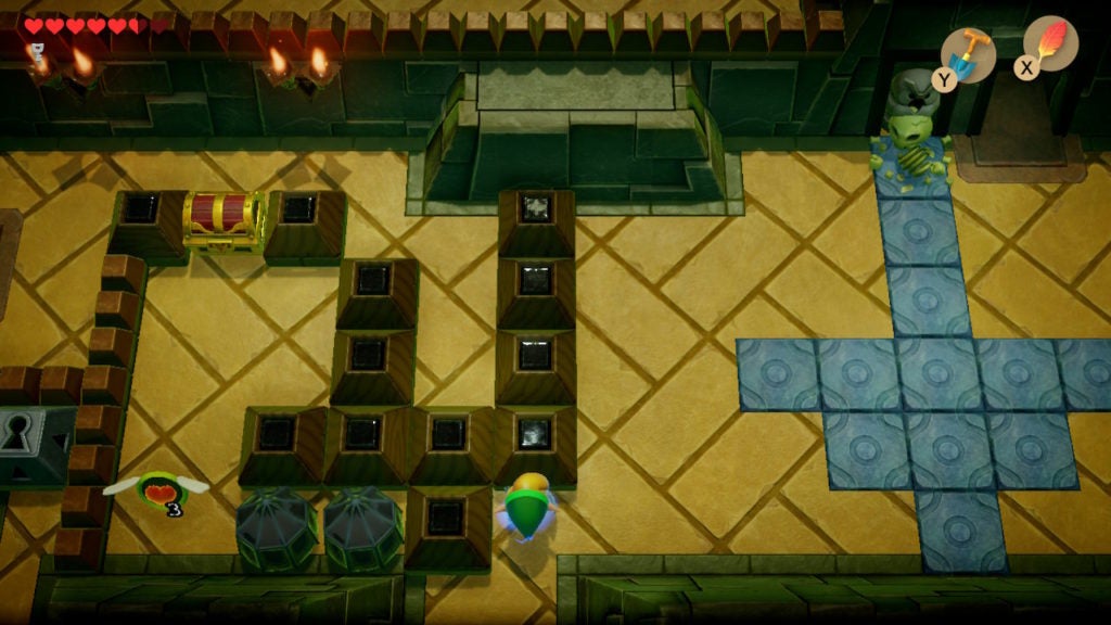 There is a chest behind some blocks, an owl statue, and a blue arrow made of floor tiles.