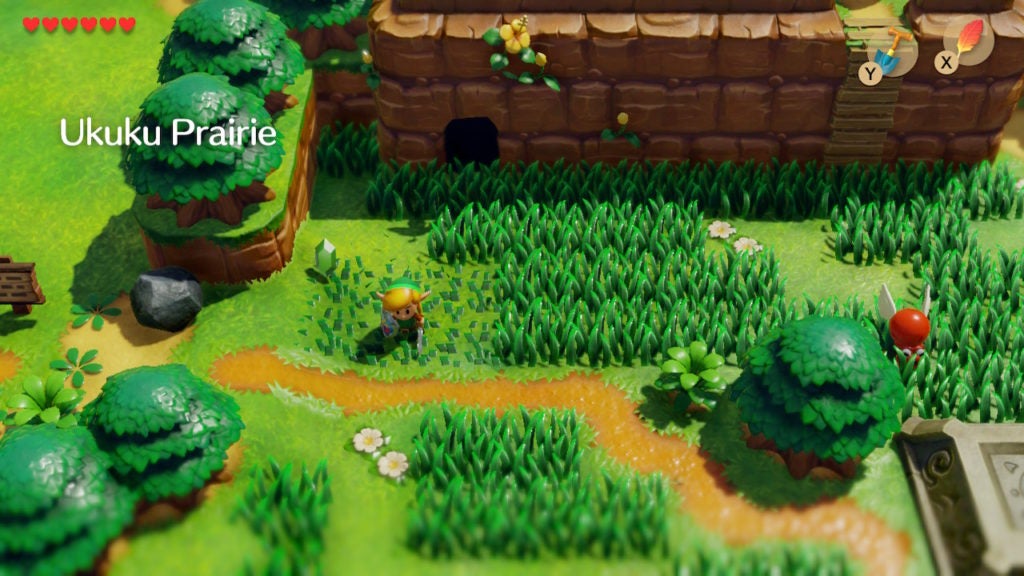 Link standing in front of a cave entrance in a grassy field.