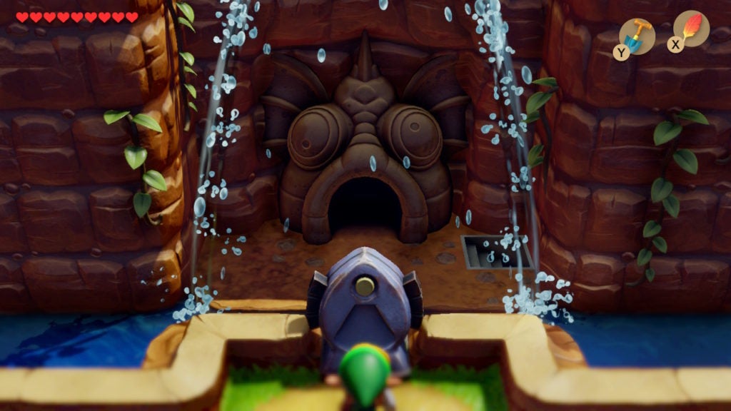 Link watching a waterfall north of Tal Tal Heights separating to reveal the entrance to the next dungeon in the wall of the cliff. The entrance is in the shape of a fish head and the entryway leads into the mouth.