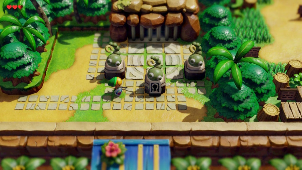 Link looking at 3 statues of worm-like creatures. The middle statue has a keyhole in it.