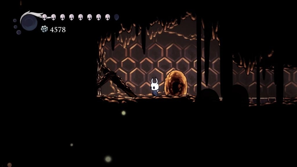 The Knight standing next to a wooden beam that unlocks a shortcut in The Hive.