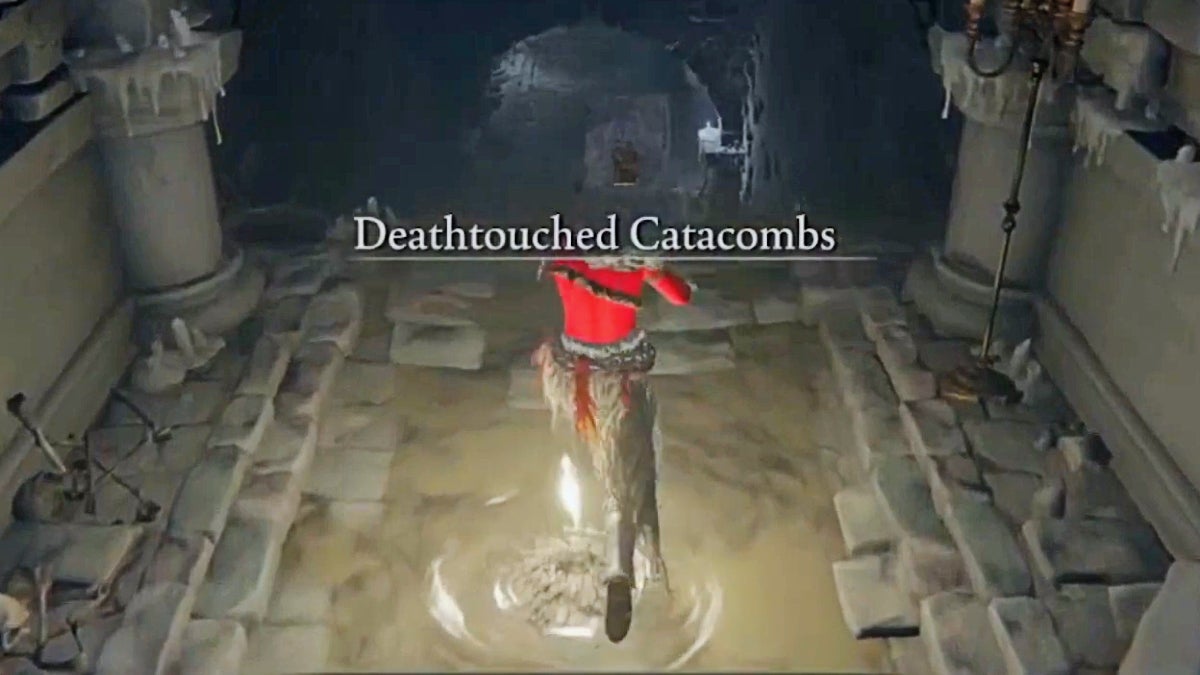 A player witha hammer standing near the site of grace in the Deathtouched Catacombs. The name text of the dungeon appears on screen.