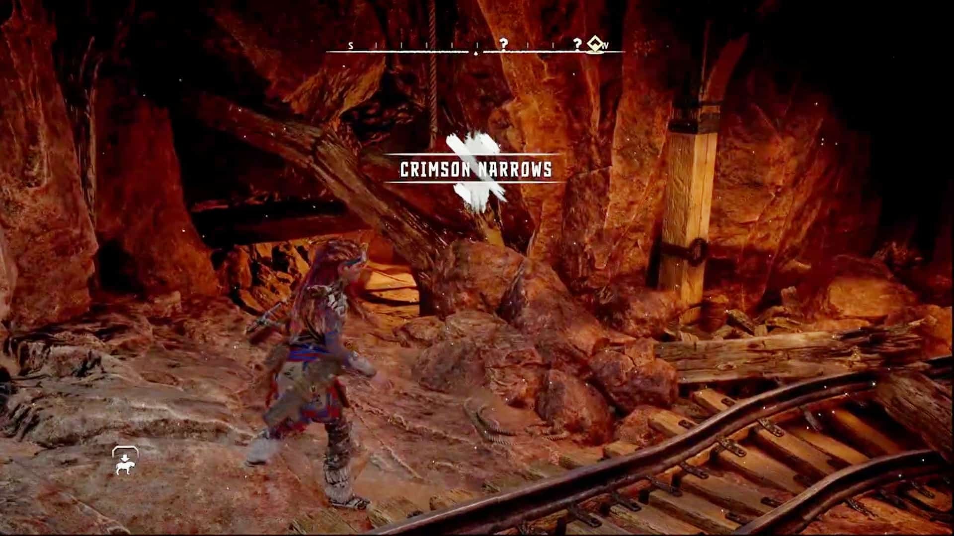 Aloy entering the Crimson Narrows mine. The rocks are dark red and there are rail tracks nearby.