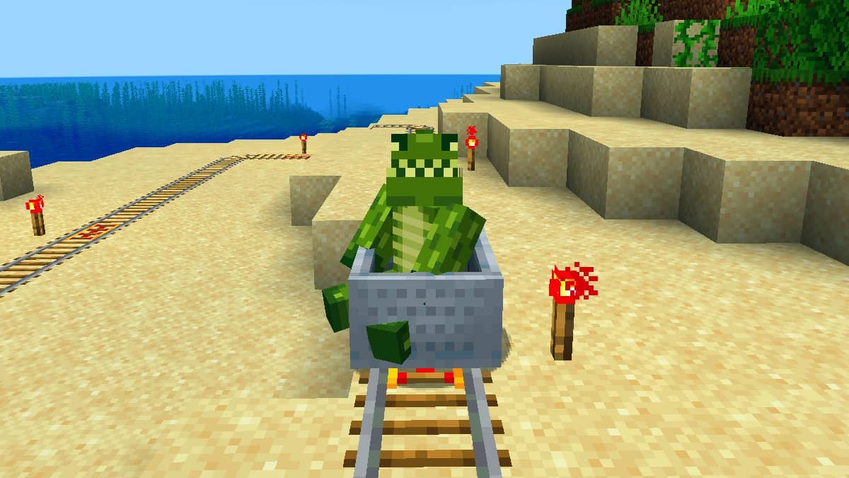 A player in a crocodile skin riding in a minecart over some powered rails on a beach.