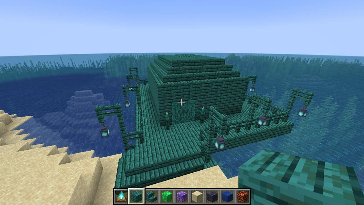 A player looking at a warped wood plank building from above with many different blocks in their hotbar.