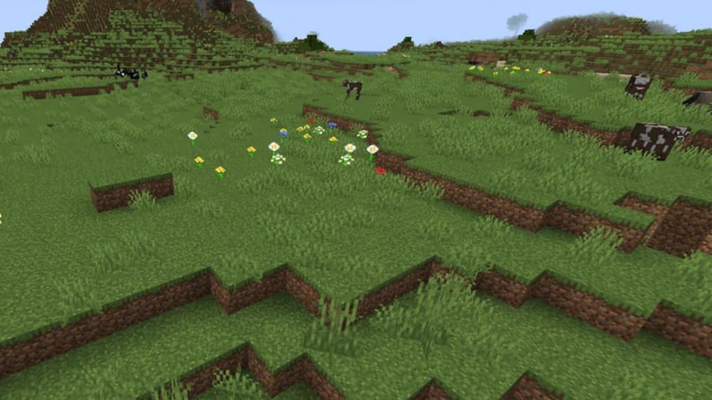 A mostly flat area with grass, flowers, and cows.