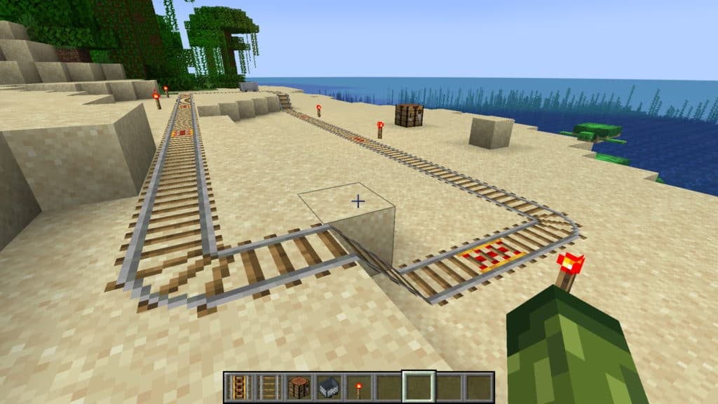A small rail system on a beach made from rails, powered rails, and redstone torches in a rectangular loop.