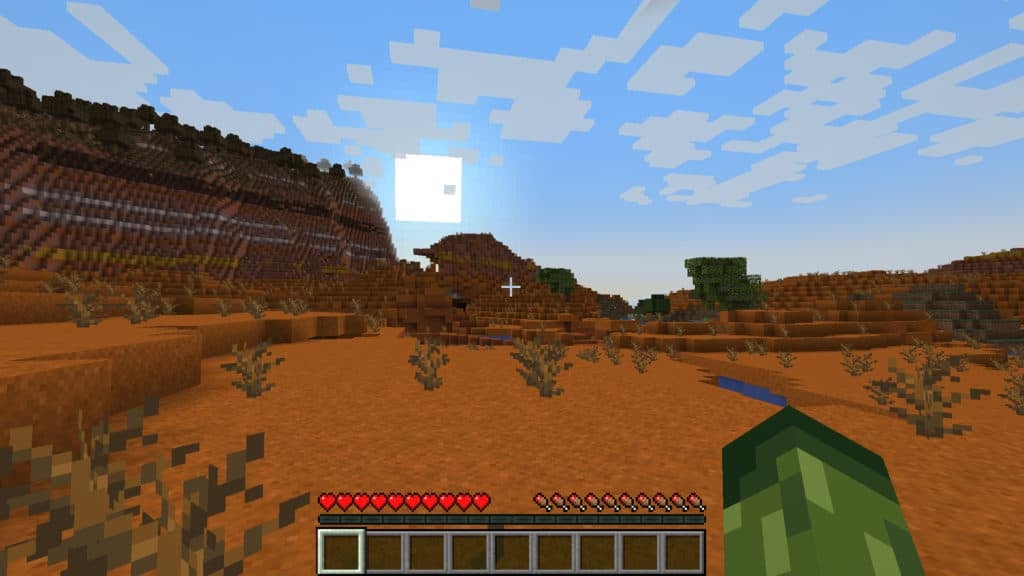 The player in first-person view looking at a rising sun cresting over a hill in a badlands biome.