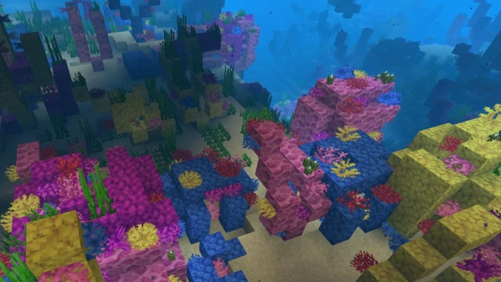 An underwater view of a warm ocean with lots of colorful coral blocks in sight. The coral is mostly pink, but there are yellow and blue growths as well.