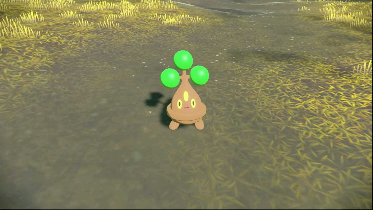 A Bonsly standing in an area with dry grass with a happy expression on its face.