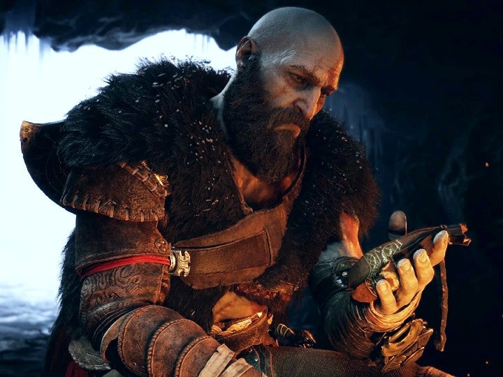 Kratos sitting in a cave and looking at a small pouch in his hand.