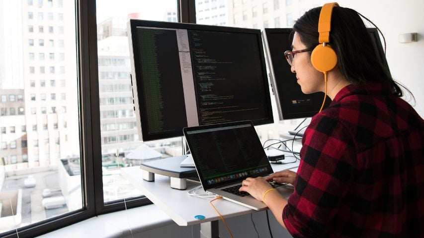 A woman coding in front of multiple computer screens