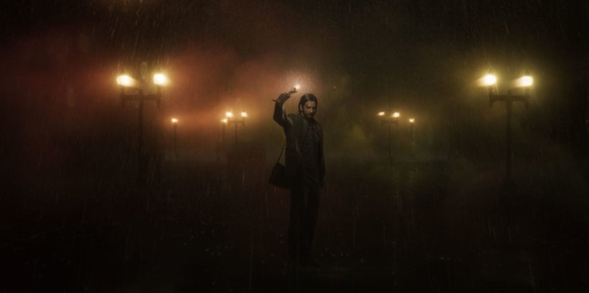 The protagonist of Alan Wake 2 standing in the rain at night while holding up a source of light.