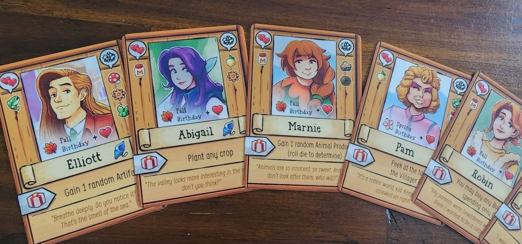 Villager cards from the Stardew Valley board game resting on a wooden table.