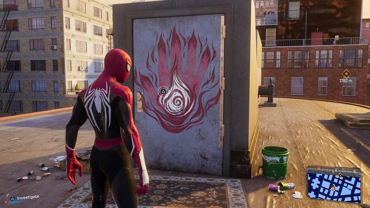 Peter standing outside the Fire Cult's base in Spider-Man 2. The door of the base has graffiti of a large red hand that looks like it's made of fire.