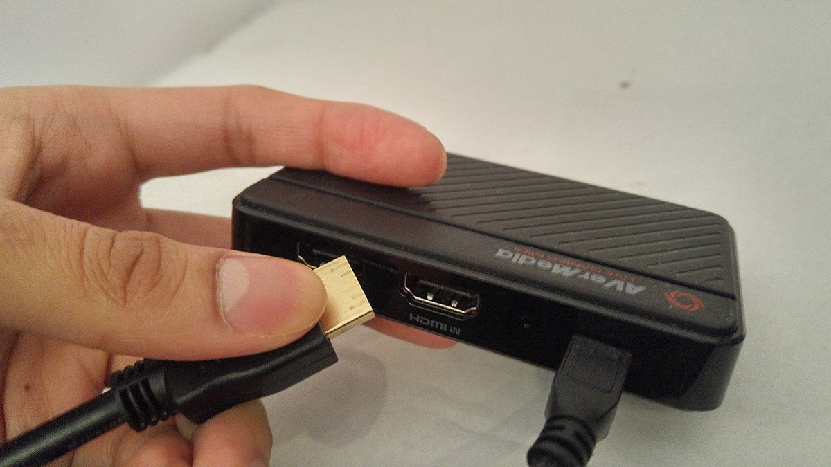 A hand holding a capture card and the end of an HMDI cable in a way that shows the HDMI In port of the capture card.