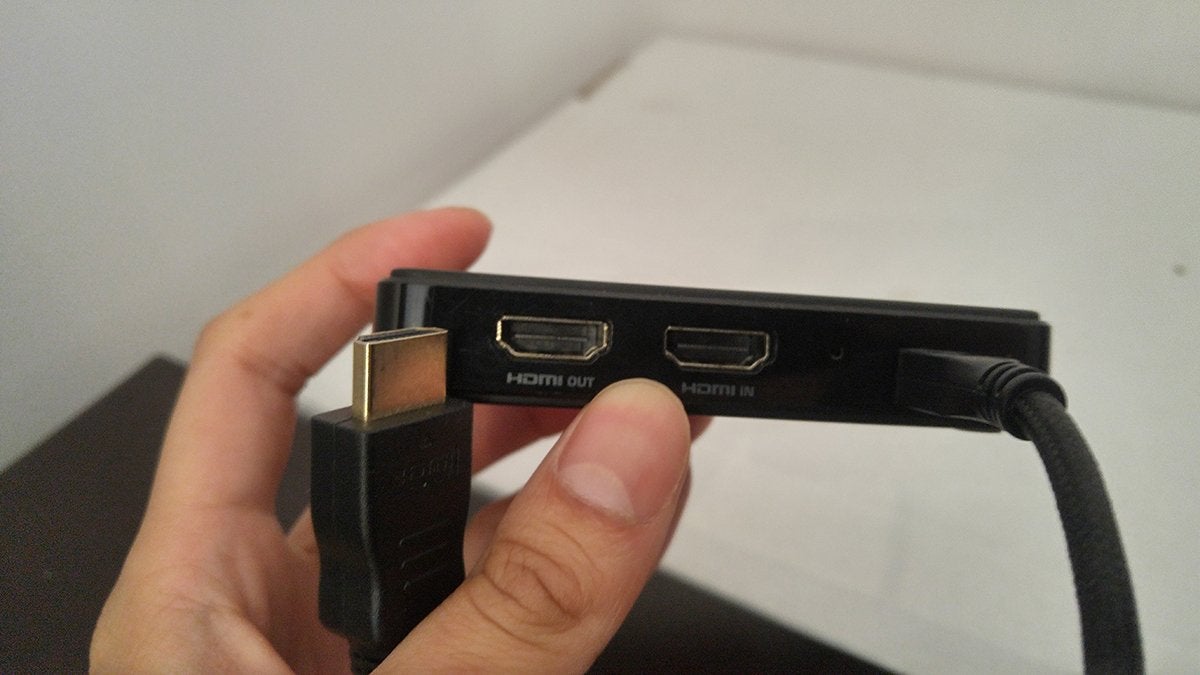A hand holding a capture card and the end of an HMDI cable in a way that shows the HDMI Out port of the capture card.