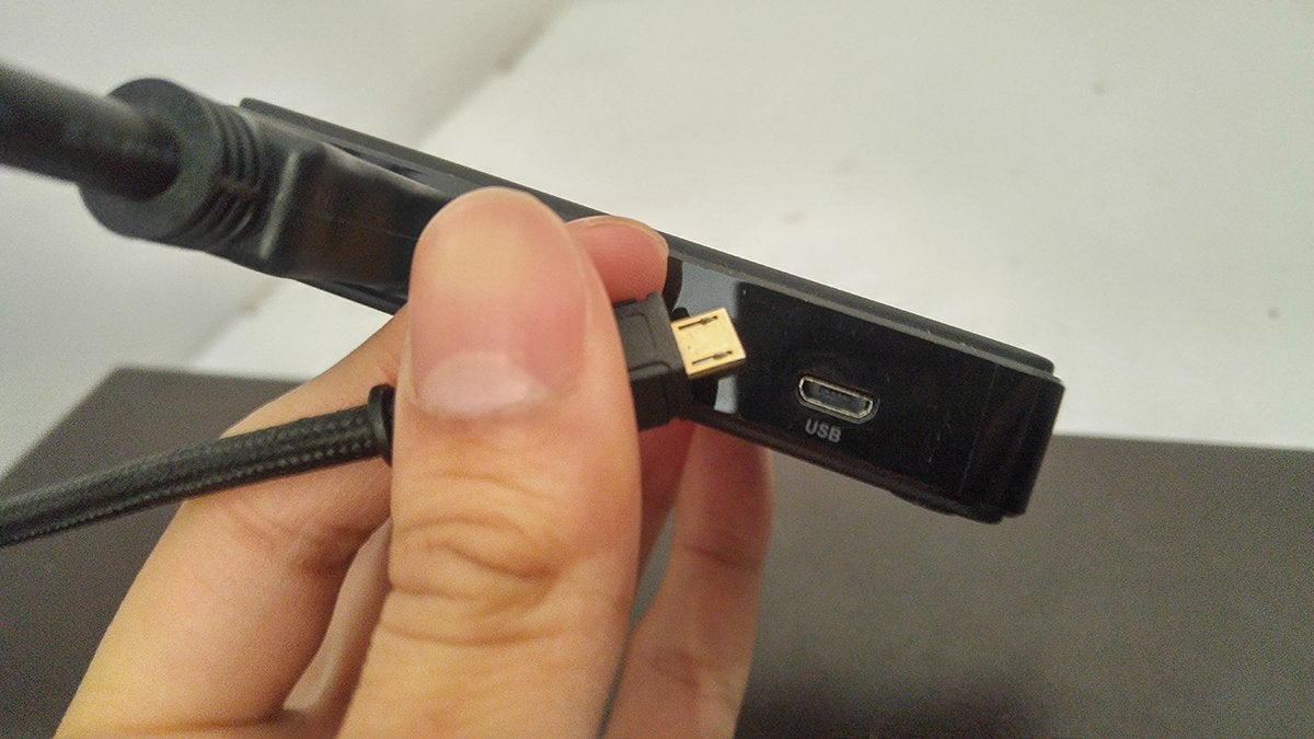 A hand holding a capture card and the end of a micro USB cable in a way that shows the micro USB port of the capture card.