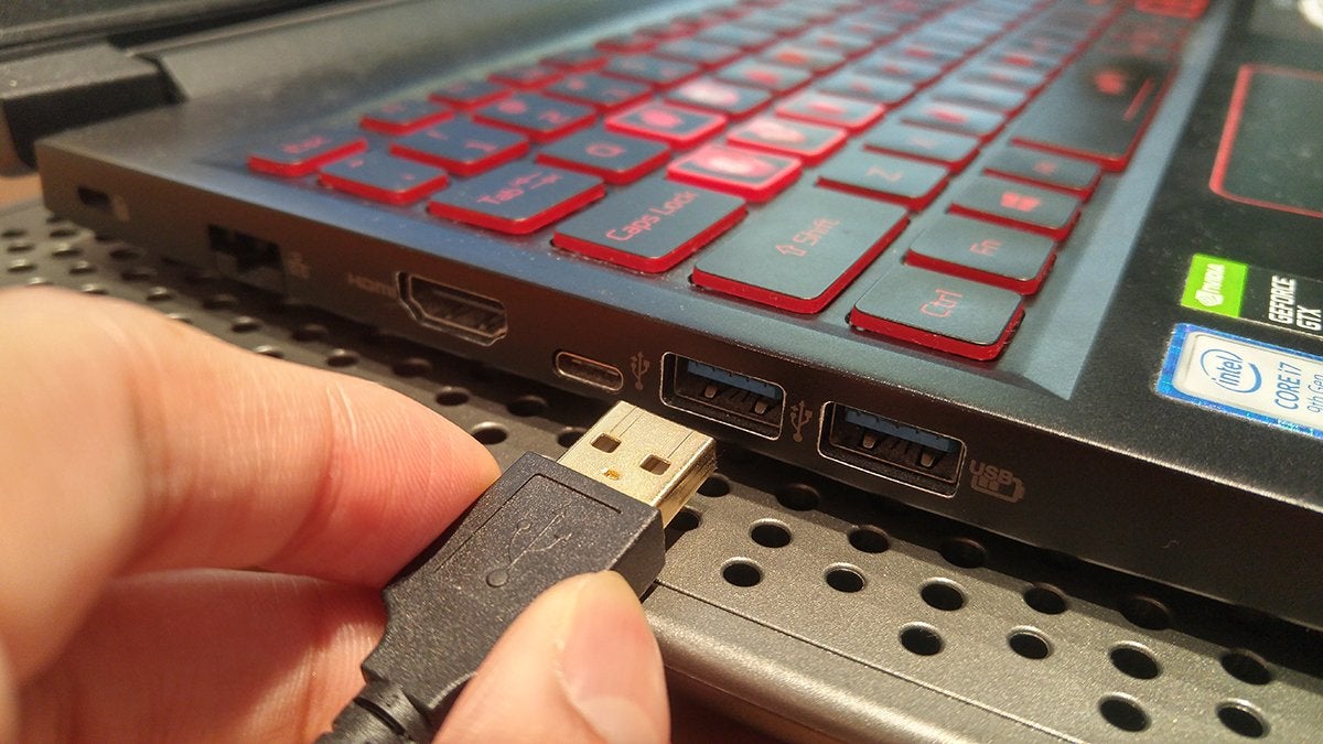 A hand about to plug the end of an USB-A cable into the USB port of a laptop.