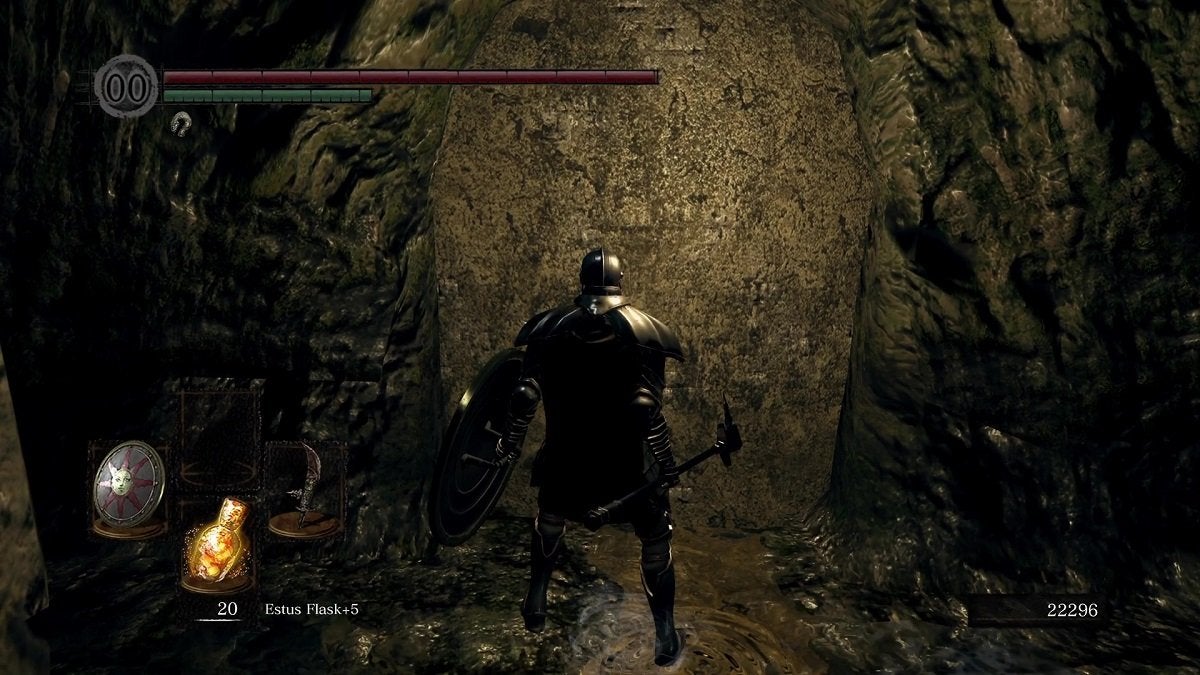 The Chosen Undead standing before an illusory wall that looks like a rough stone slab in a cave.