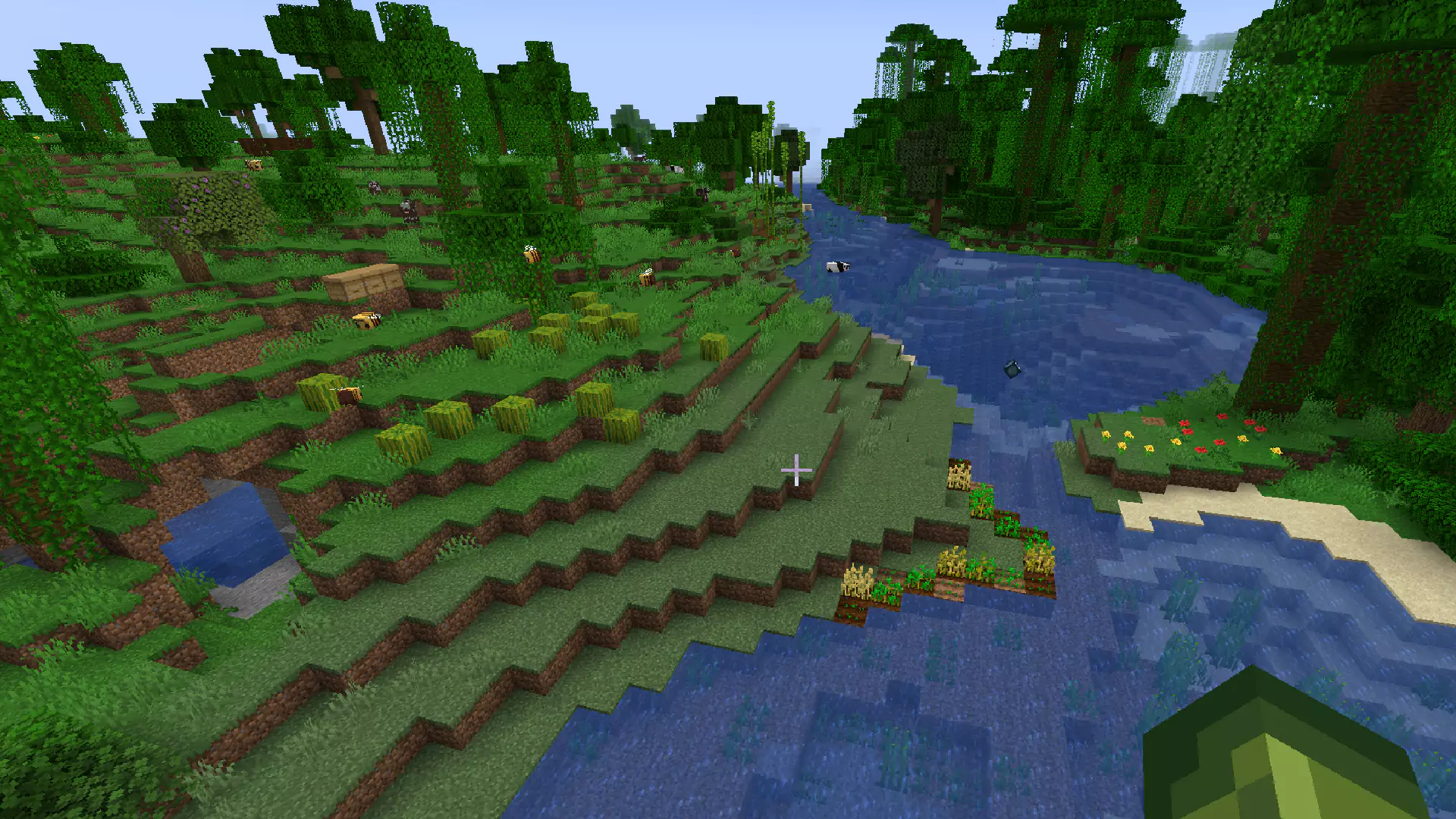 Beehives on a hill to the left, crops in the middle, and flowers to the right across a river.